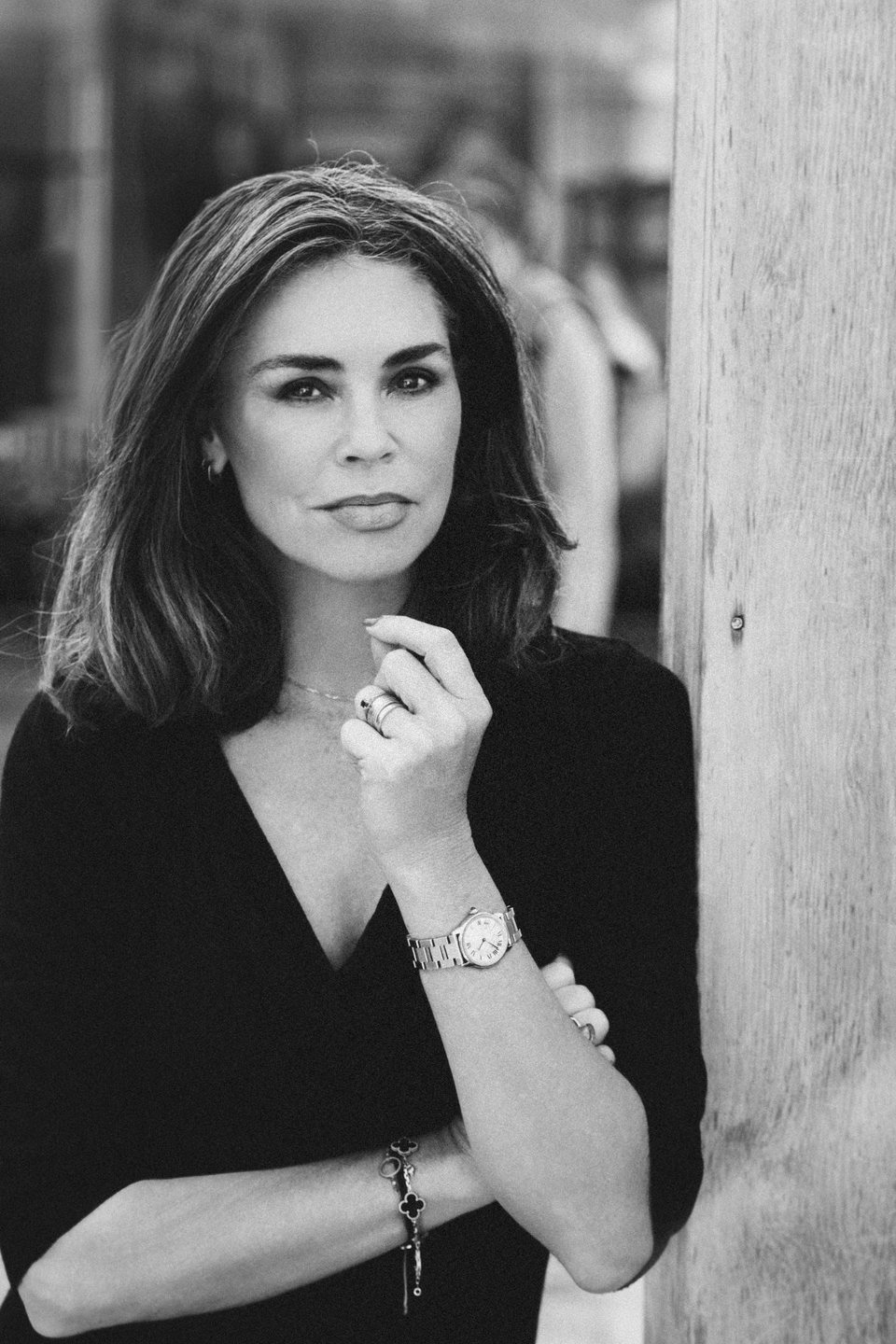 Tara in a black dress, one hand at her collarbone, looking at the camera.